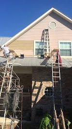 A man is painting the side of a house with a ladder.
