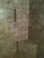 A tiled shower with a bench and a shelf.
