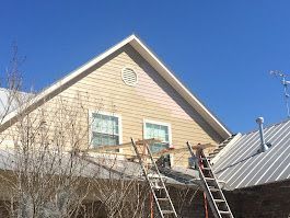 A man is standing on a ladder on the roof of a house.
