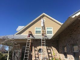 A man is standing on a ladder painting the side of a house.