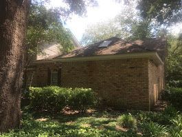 A brick house with a skylight on the roof is surrounded by trees and bushes.