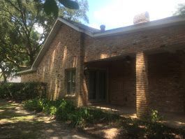 A brick house with a porch and a chimney on the roof.