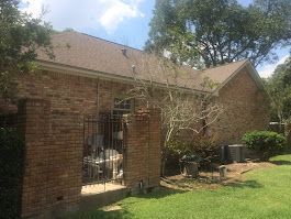 A brick house with a brown roof and a fence in front of it.