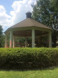 A gazebo is surrounded by bushes and trees in a park.