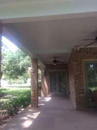 There is a ceiling fan on the porch of a brick house.
