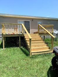 A wooden deck with stairs leading up to it is in front of a mobile home.