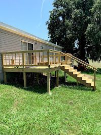 A wooden deck with stairs leading up to it is in front of a mobile home.