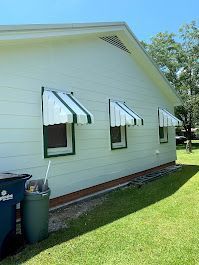 A white house with green and white awnings on the windows.