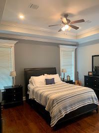 A bedroom with a bed, dresser, nightstand, and ceiling fan.