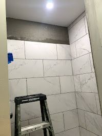 A bathroom with white tiles and a ladder in the corner.