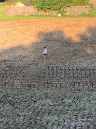 A boy is standing in the middle of a muddy field.