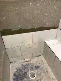 A bathroom with white tiles being installed on the wall and floor.