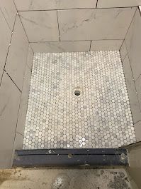 A shower stall with white tiles and a hole in the floor.