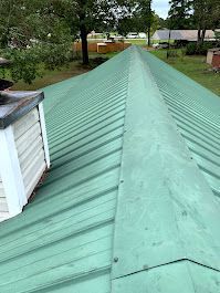 A green metal roof with a white chimney on top of it.
