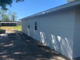 A white house with a lot of windows is sitting on top of a dirt field.