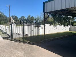 A wrought iron gate is surrounded by a white wall and grass.