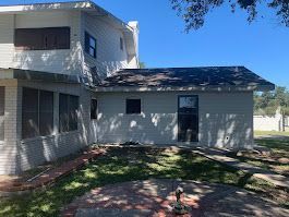 A large white house with a black roof is sitting in the middle of a lush green field.