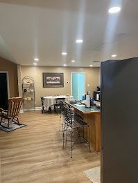A living room with hardwood floors , a table , chairs , and a refrigerator.
