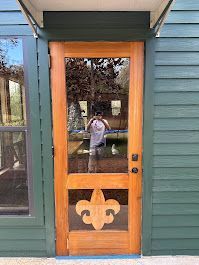 A wooden door with a fleur de lis on it is on a green house.
