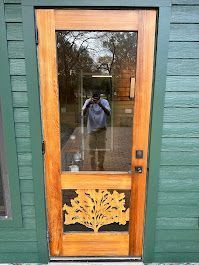 A man is taking a picture of himself in a mirror in front of a wooden door.