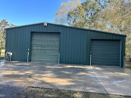 A green metal building with two garage doors and a driveway.