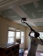 A man is painting the ceiling of a room with a sander.