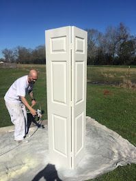A man is painting a white folding door in a field.
