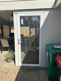 A white screen door is sitting next to a green trash can.