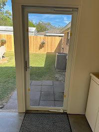 A sliding glass door leading to a backyard with a dog in the background.