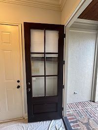 A black door with glass panels is sitting in a room next to a white door.