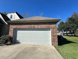 A white garage door is sitting in front of a brick house.