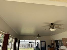 A living room with a ceiling fan and a lot of windows.