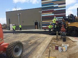 A group of construction workers are working on a road in front of a building.