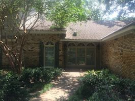 A brick house with a walkway leading to the front door surrounded by trees and bushes.