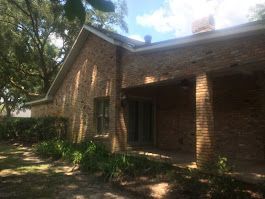 A large brick house with a porch and trees in front of it.