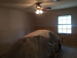 A room with a car covered in plastic and a ceiling fan.