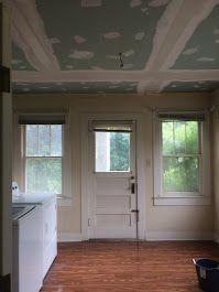 An empty room with a ceiling that is being painted and a door.