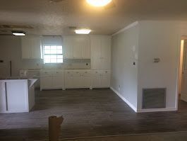 An empty kitchen with white cabinets and hardwood floors in a house.