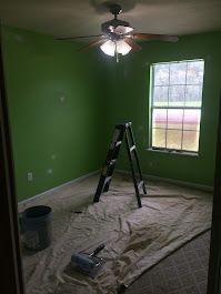 A room with green walls and a ceiling fan is being painted.