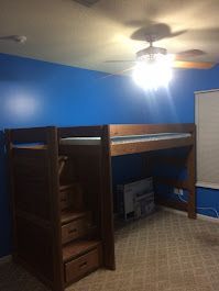 A bunk bed with stairs and drawers in a room with blue walls.
