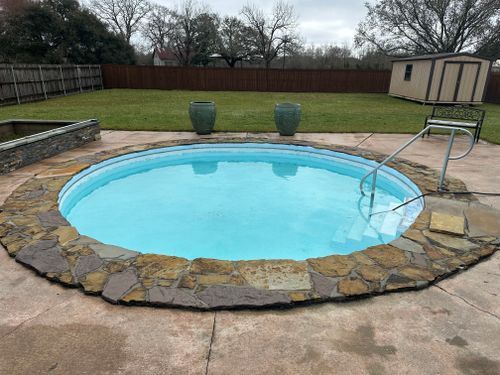 A round swimming pool surrounded by rocks in a backyard.