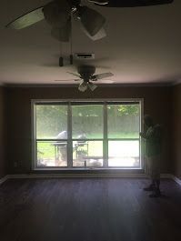 An empty living room with a ceiling fan and a large window.