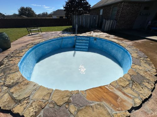 A swimming pool is surrounded by stone and has stairs leading to it.