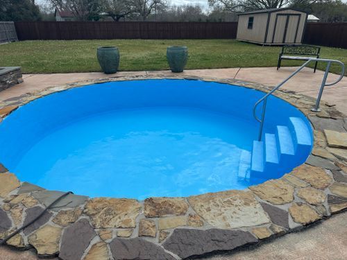A blue swimming pool with stairs leading to it in a backyard.