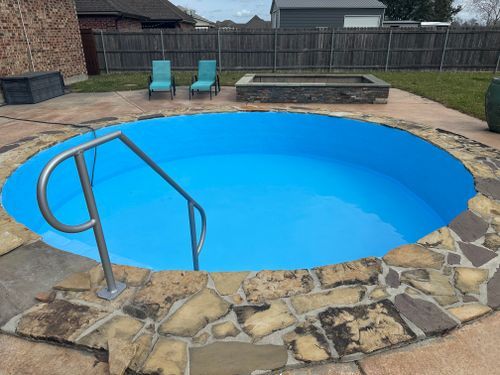 A blue swimming pool with stairs leading to it in a backyard.