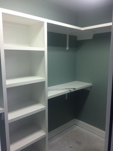 A walk in closet with white shelves and a desk.