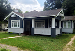 A small black and white house with a porch is sitting on top of a lush green lawn.