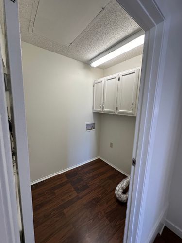 A laundry room with hardwood floors and white cabinets.