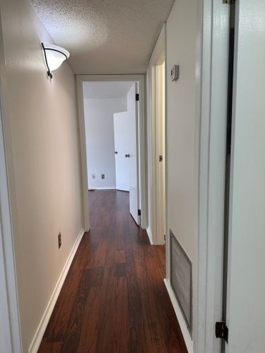 A hallway with hardwood floors and white walls leading to a bedroom.