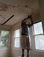 A man is working on the ceiling of a room with a drill.